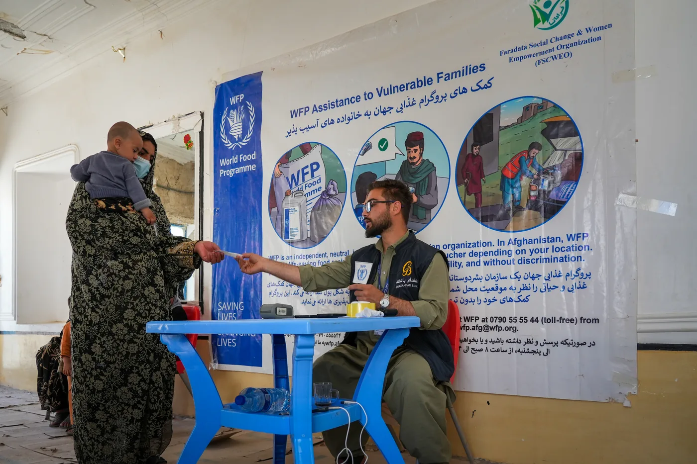 A woman and child meet staff at a WFP food assistance desk in Farah