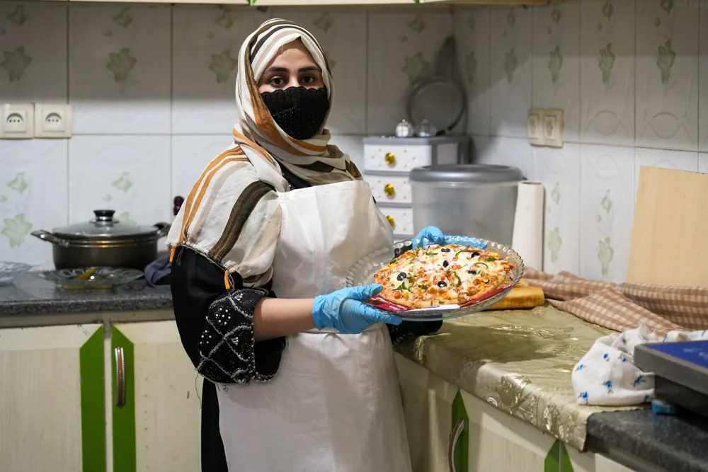 A woman holds prepared food in a small commercial kitchen