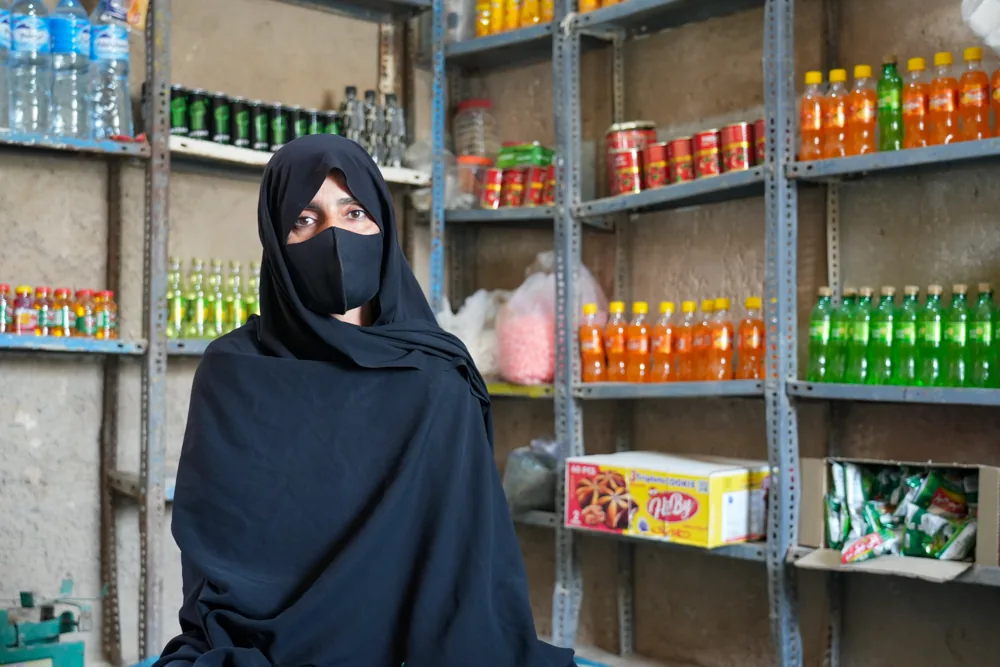 A woman stands beside stocked shelves in a small shop